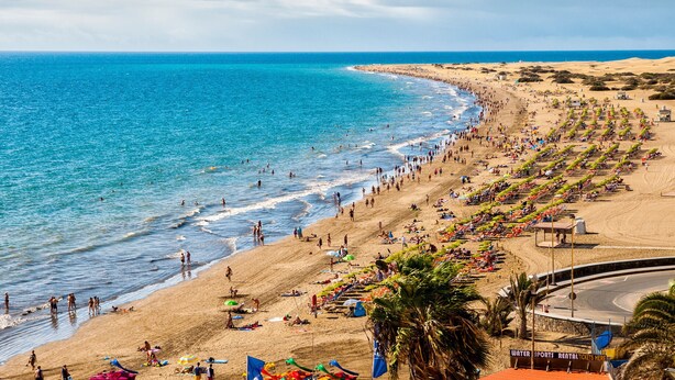 A beach with a curved road, palm trees, and people enjoying the water. - PRIVATE HEATED POOL - Fully refurbished in 2022 (San Bartolomé de Tirajana)