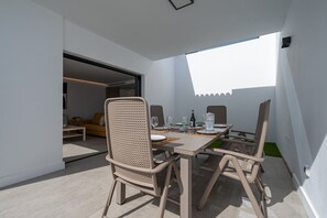 Un espace repas moderne avec une table dressée pour quatre personnes, entourée de chaises en osier, et une vue sur un balcon doté d’une balustrade blanche.
