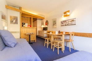 A room with a bed, a dining table with chairs, a kitchen area, and artwork on the walls.