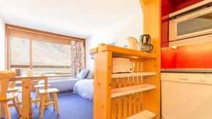 Una stanza accogliente con un tavolo da pranzo in legno, sedie, un letto con vista, uno scaffale a incasso e un frigorifero bianco.