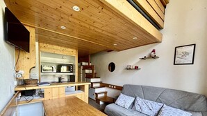 Un espacio habitable compacto con una mesa de comedor de madera, un sofá gris y una zona de kitchenette.