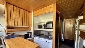 Cocina compacta con muebles de madera, microondas, lavaplatos y fregadero.