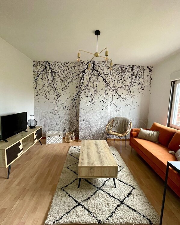 A modern living room with a wooden coffee table, a sofa, a TV, and a wall with a tree branch design.