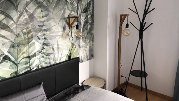 A bedroom with a bed, a wall-mounted light fixture, and a floor lamp.
