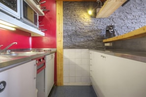 Een kleine keuken met een rode wand, een steenschild en een koffieapparaat.