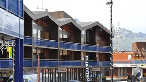 A multi-story building with balconies, a sign for 'Centre Médical', and a mountain backdrop.
