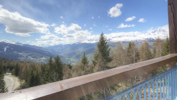 A balcony with a view of snow-capped mountains and a forested valley.