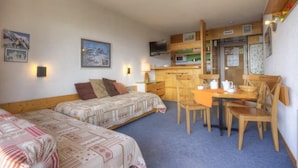 A room with two beds, a dining table with chairs, a microwave, and a small kitchen area.