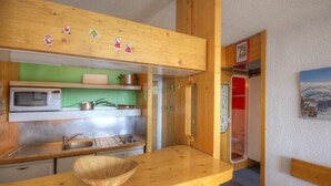 A compact kitchen with wooden cabinets, a microwave, a sink, and a small window.