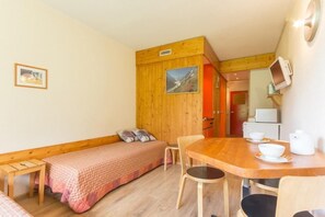 A small, cozy room with a wooden bench, a single bed, a wooden dining table with chairs, and a television mounted on the wall. - 50m from resort center, 1st floor, view valley, balcony, tv, 24m², Les Arcs (Les Arcs)