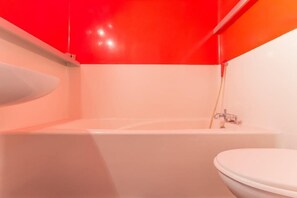 Ein modernes Badezimmer mit einer weißen Badewanne, einem weißen Waschbecken und einer roten Akzentwand.