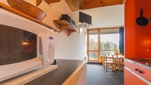 Una cucina con forno a microonde, scaffali in legno, una televisione e un'area pranzo con tavolo e sedie.