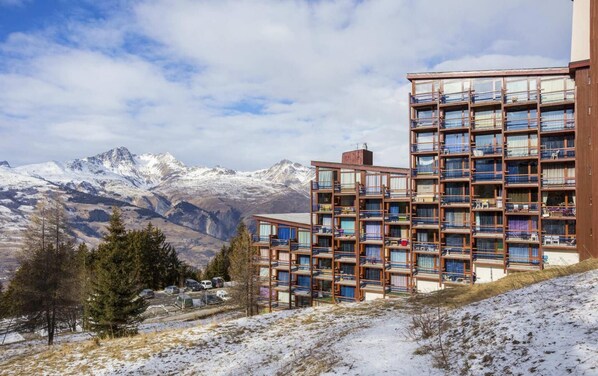 A multi-story building with balconies, set against a backdrop of snow-capped mountains.