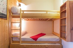 A bunk bed with a ladder, a red blanket, and a wooden shelf unit.