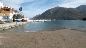 Una marina costera con barcos amarrados, una playa arenosa y montañas al fondo.