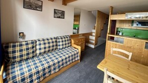 A cozy room with a plaid sofa, wooden dining table, and a kitchen area with green cabinets.