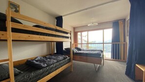 A dormitory room with bunk beds, a window with curtains, and a view of the outdoors.