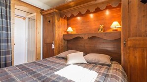 Een houten bed met een ruitdessin sprei, twee nachtlampjes en een decoratief object op het hoofdeinde.