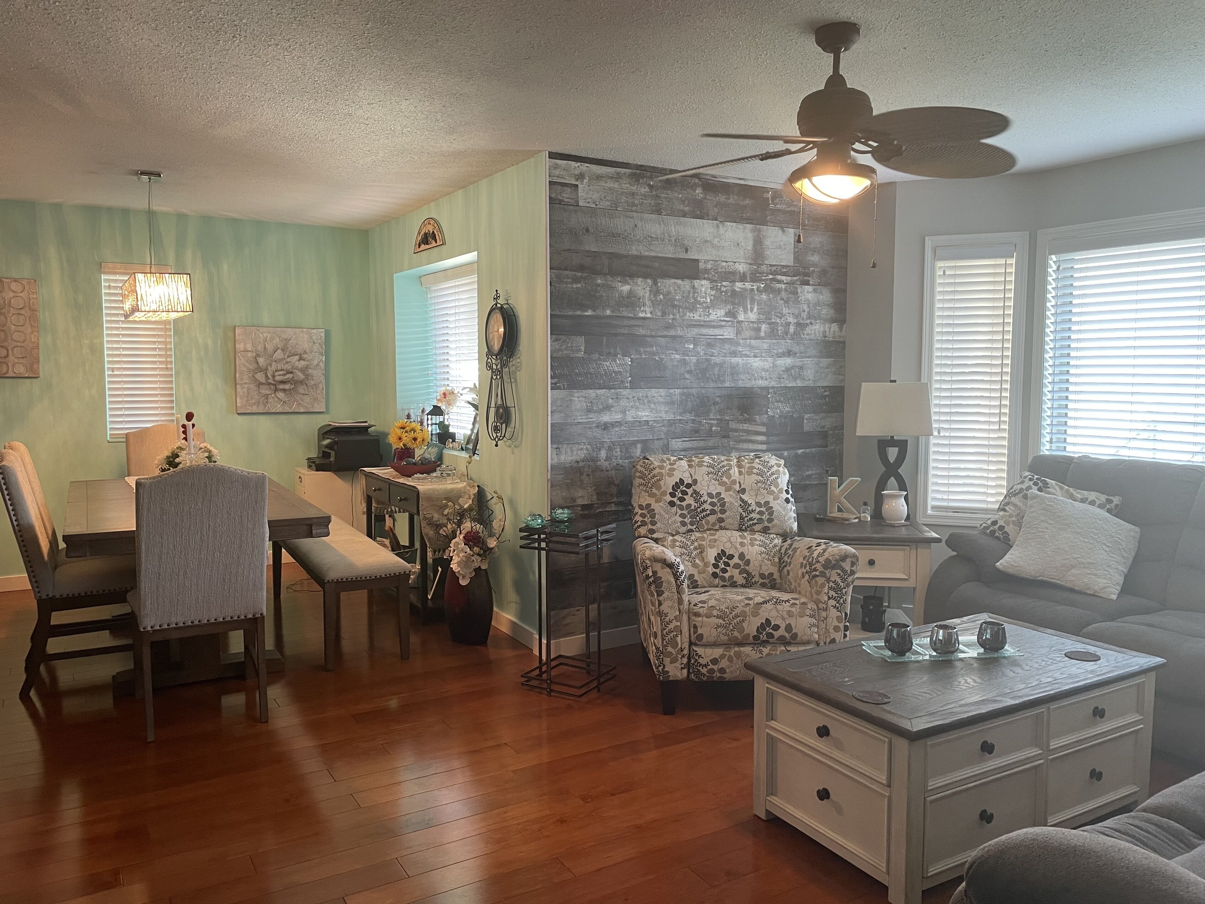 A living room with a dining area, wooden flooring, a ceiling fan, and a sofa.