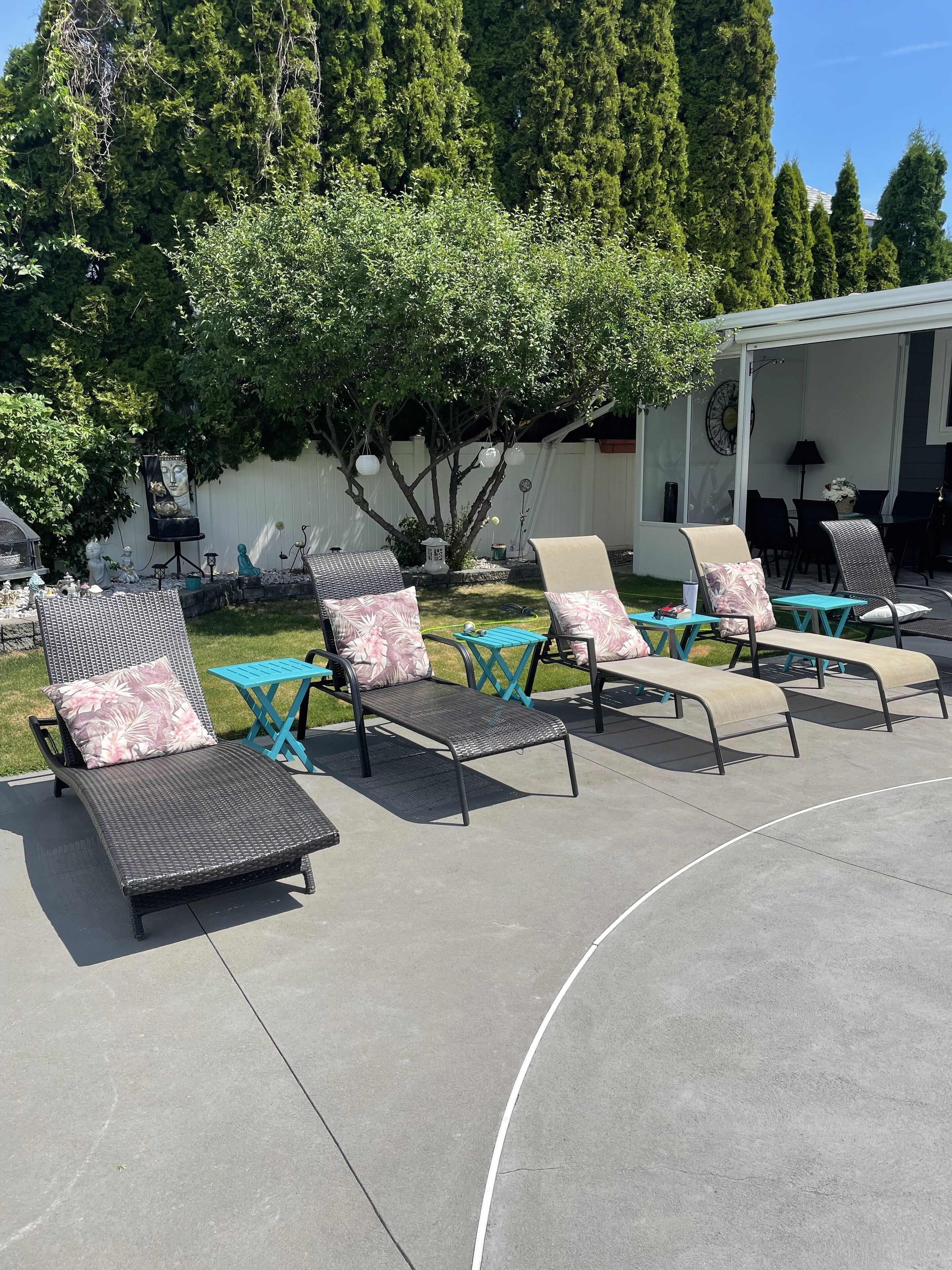 Eine Terrasse mit Liegestühlen und einem kleinen Tisch, umgeben von Grünpflanzen und einem weißen Zaun.