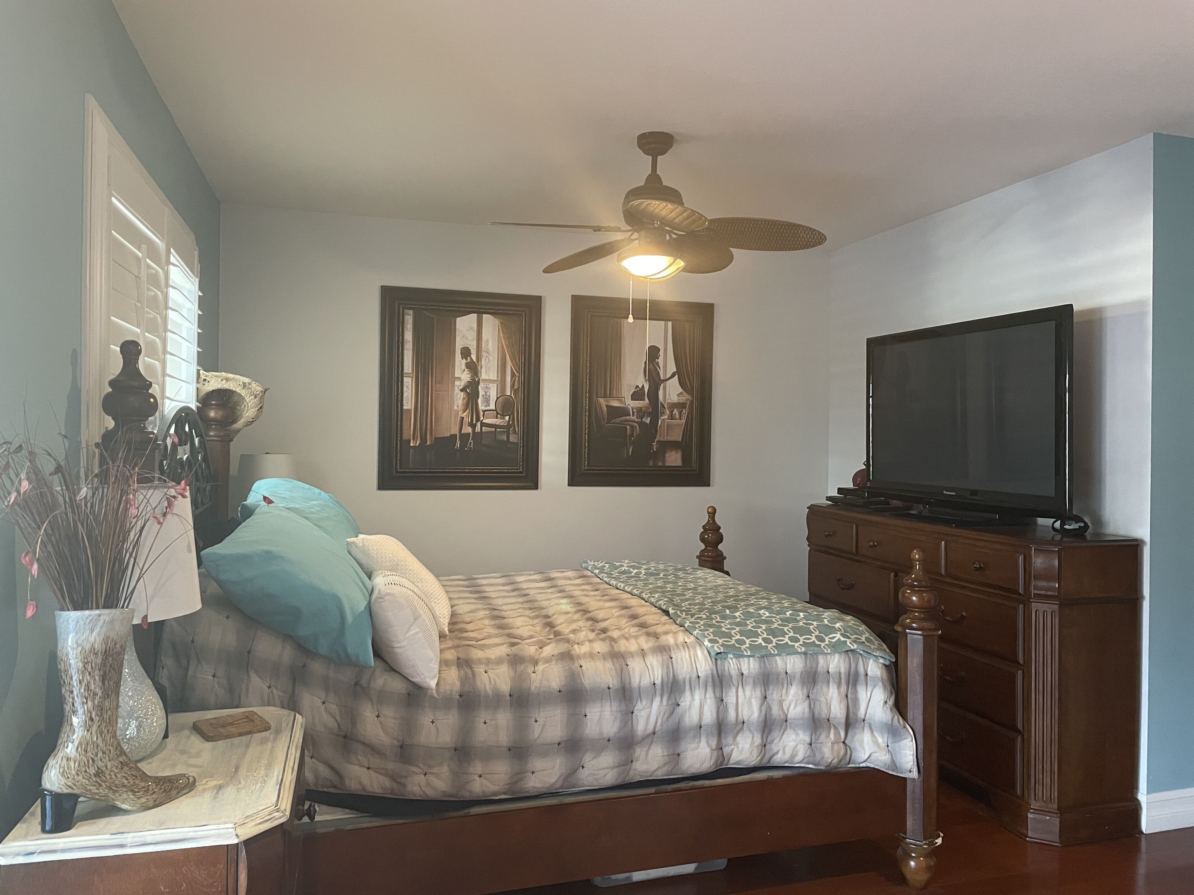 A bedroom with a bed, a dresser, a ceiling fan, and a TV.