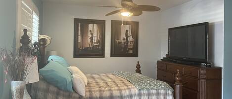A bedroom with a bed, a dresser, a ceiling fan, and a TV.
