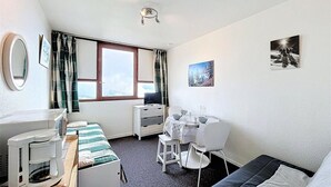 A compact hotel room with a bed, a desk with a chair, a small table, a microwave, and a window with curtains. - 50m from ski slopes, 9th floor, view valley, swimming pool, tv, ski locker, 16m², Le Corbier (Le Corbier)