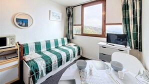 A small, tidy room with a bed, a desk with a computer, a window with curtains, and a view of the outdoors. - 50m from ski slopes, 9th floor, view valley, swimming pool, tv, ski locker, 16m², Le Corbier (Le Corbier)