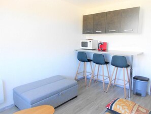 A compact living space with a kitchenette, grey sofa, two bar stools, and a small trash bin. - 10m from resort center, 6th floor, view valley, swimming pool, tv, ski locker, 16m², Le Corbier (Le Corbier)