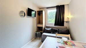Ein kleiner Wohnbereich mit Sofa, Tisch, Fernseher und einem Fenster mit Vorhängen.