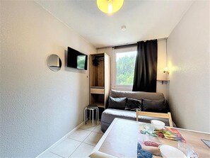 A compact living space with a sofa, a small table, a TV, and a window with curtains. - 10m from resort center, 10th floor, view ski slopes, swimming pool, tv, ski locker, 14m², Le Corbier (Le Corbier)