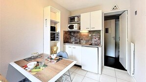 Eine kleine Küche mit weißen Schränken, einer Mikrowelle und einem Spülbecken. Es gibt einen Esstisch mit Stühlen und einen kleinen Kühlschrank.