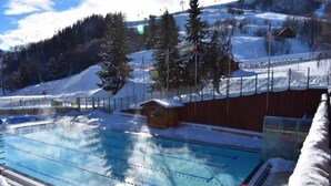 Ein Schwimmbad mit Holzterrasse und einer kleinen Holzhütte in einer verschneiten Berglandschaft.