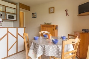 A kitchen with a dining table set for four, wooden chairs, a microwave, and a cabinet. - 10m from resort center, 6th floor, view ski slopes, swimming pool, balcony, tv, ski locker, 24m² (Le Corbier)