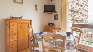 A dining area with a wooden cabinet, a TV on a shelf, and a view of a residential building through a window. - 10m from resort center, 6th floor, view ski slopes, swimming pool, balcony, tv, ski locker, 24m² (Le Corbier)