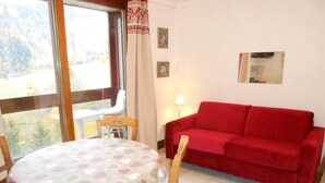 A room with a dining table covered with a patterned tablecloth, a red sofa, and a window with curtains. - 10m from resort center, 6th floor, view ski slopes, swimming pool, balcony, tv, ski locker, 24m² (Le Corbier)