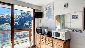 A modern kitchen with wooden cabinets, a microwave, and a toaster. There is a large window offering a view of a mountainous landscape. - 100m from ski slopes, 12nd floor, view ski slopes, swimming pool, balcony, tv, ski locker, 22m² (Le Corbier)