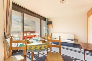 A room with a large window, a bed, a dining table with chairs, and a small table with a television. - 10m from resort center, 10th floor, view ski slopes, swimming pool, balcony, tv, ski locker, 31m² (Le Corbier)