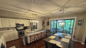 Una cocina con armarios blancos, un refrigerador de acero inoxidable y una mesa de comedor de madera con cuatro sillas.