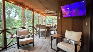 Un amplio espacio al aire libre con mesas y sillas de madera, un ventilador de techo y un televisor montado en la pared.