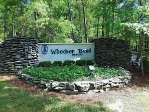 Schild für das Woodson Bend Resort, umgeben von Steinmauern und Grünpflanzen.