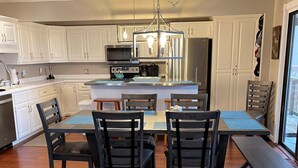 Una cocina moderna con armarios blancos, una isla central y una zona de comedor con sillas de madera y un banco.