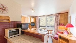A compact kitchen with a toaster, wooden cabinets, a window with curtains, and a small dining area. - 50m from ski slopes, 4th floor, view ski slopes, swimming pool, balcony, tv, ski locker, 31m² (Le Corbier)