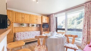 A cozy room with wooden furniture, a dining table, and a large window offering a view of the outdoors. - 50m from ski slopes, 4th floor, view ski slopes, swimming pool, balcony, tv, ski locker, 31m² (Le Corbier)