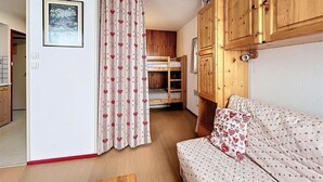 A cozy room with a bunk bed, wooden cabinets, a sofa with a floral pattern, and a curtain with a heart design. - 10m from ski slopes, 6th floor, view mountain, swimming pool, tv, ski locker, 26m², Le Corbier (Le Corbier)