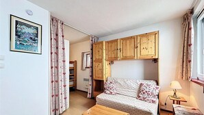 A cozy living room with a sofa, wooden cabinets, a small table, and a lamp. - 10m from ski slopes, 6th floor, view mountain, swimming pool, tv, ski locker, 26m², Le Corbier (Le Corbier)