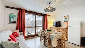 A cozy living room with a sofa, a dining table with chairs, a TV, and a refrigerator.