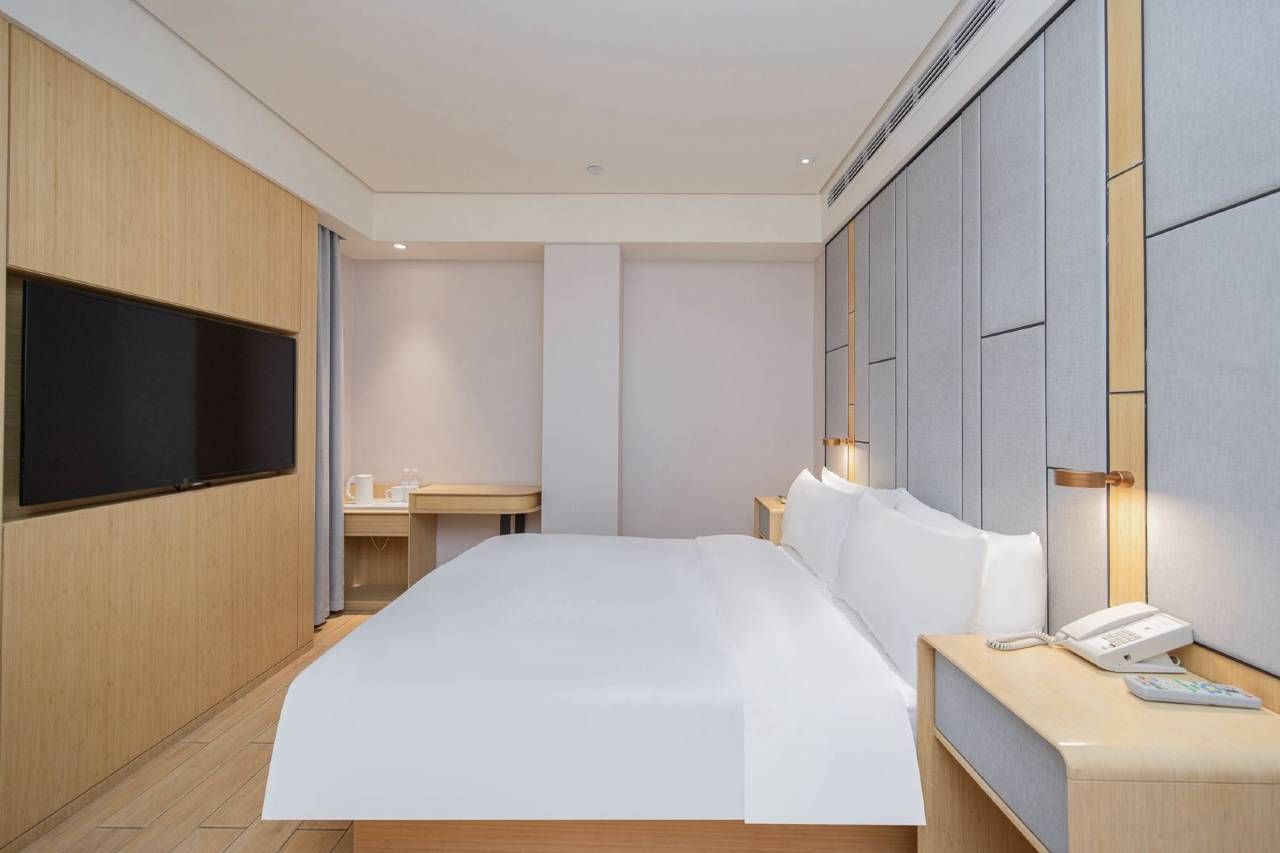 A modern hotel room with a large bed, a flat-screen TV, bedside tables, and a telephone.