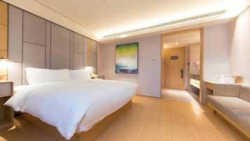 A hotel room with a large bed, bedside tables, a painting on the wall, and a door leading to a bathroom.