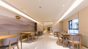 A modern interior with wooden tables and chairs, a light-colored floor, and a view through a doorway. - Ji Hotel (Nanjing)